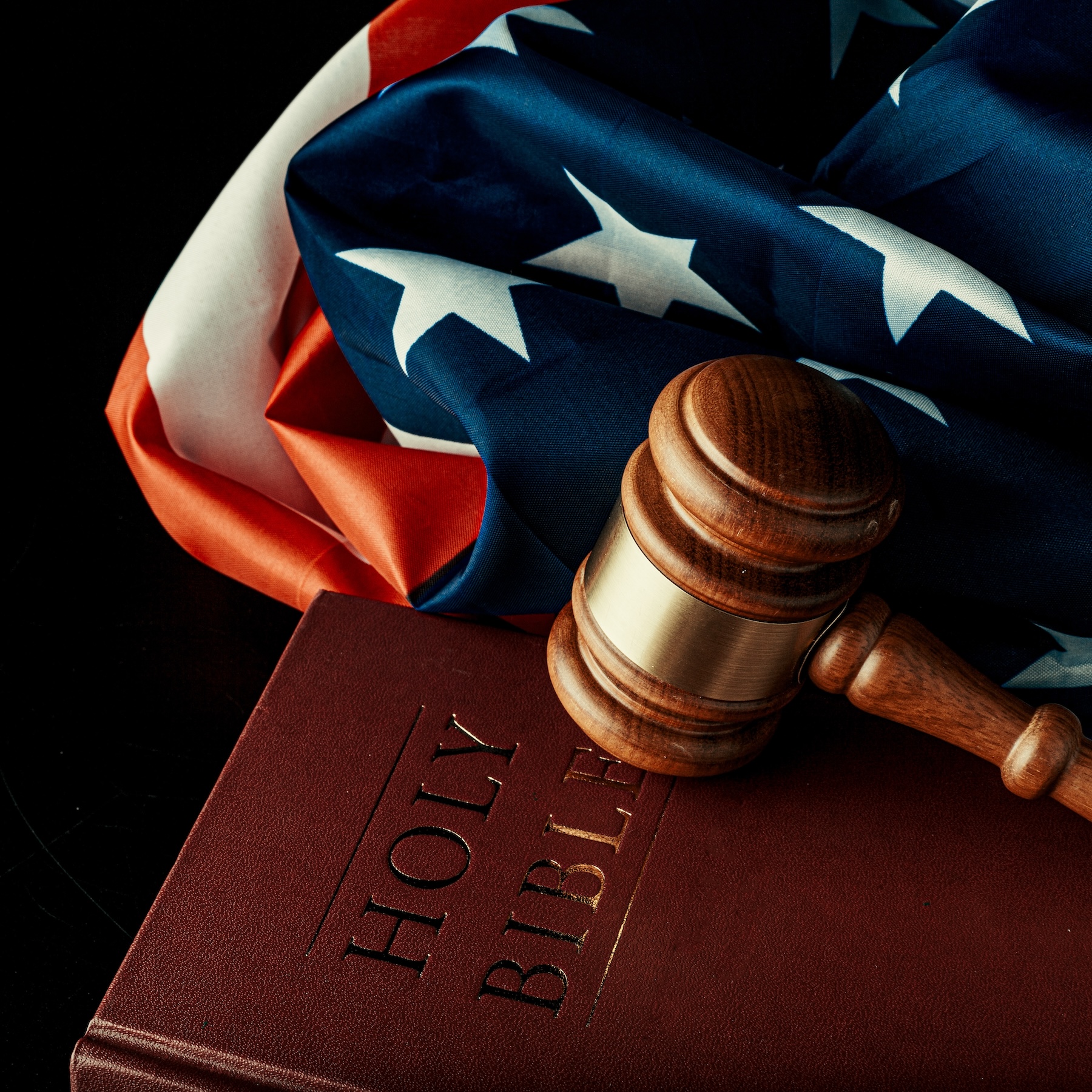 Close-up of a wooden gavel on a Bible with an American flag background, representing the ethical legal standards of The Ramsey Law Firm in Rockford, IL.